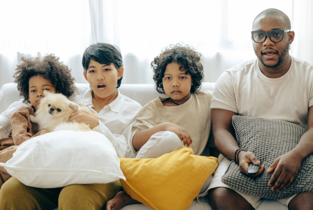A family of four sitting on a couch, engrossed in watching TV together